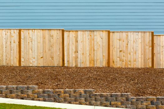 New Garden Wood Fence with house siding barkdust mulch concrete retaining wall along exterior sidewalk