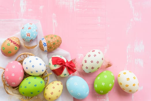 Happy easter! Colorful of Easter eggs tied with red ribbon in nest with paper star, flower and Feather on pastel color bright pink and white wooden background.