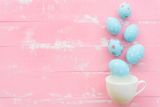 Happy easter! Row colorful Easter eggs spread out from white cup on bright pink and green wooden background.