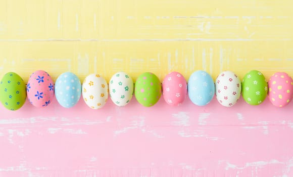 Happy easter! Row Easter eggs with colorful paper flowers on bright pink and yellow wooden background.