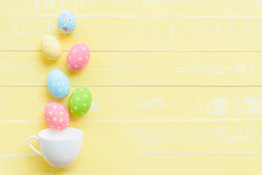 Happy easter! Row colorful Easter eggs spread out from white cup on bright yellow wooden background.