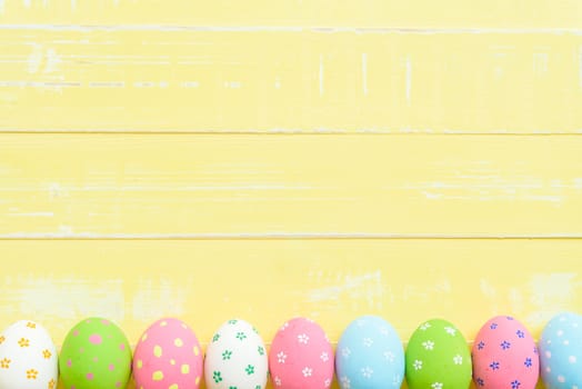 Happy easter! Row Easter eggs with colorful paper flowers on bright yellow wooden background.