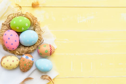 Happy easter! Colorful of Easter eggs in nest with red ribbon, Feather and paper star on pastel color bright yellow and white wooden background.