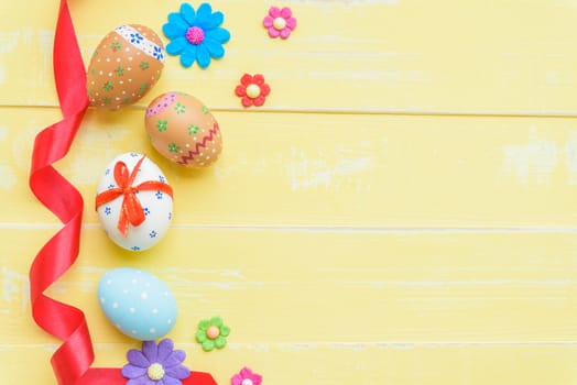 Happy easter! Colorful of Easter eggs in nest with red ribbon, Feather and paper star on pastel color bright yellow and white wooden background.