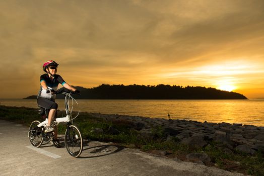 Silhouette of a senior woman cyclist at sunset or sunrise near ocean