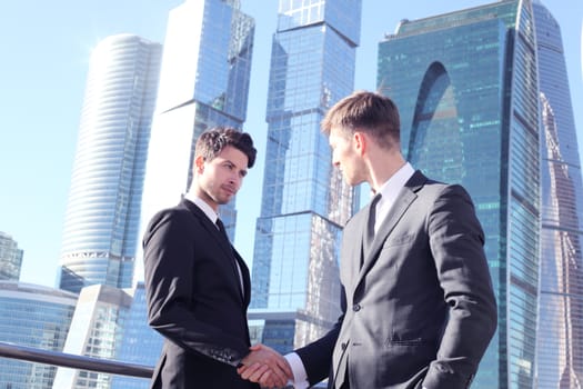 Business people shaking hands on skyscraper background