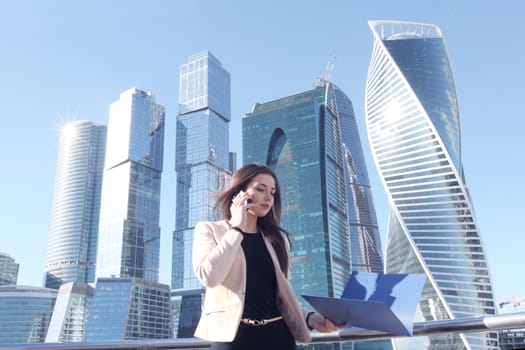 Young beautiful businesswoman with cellphone outdoors at skyscraper background