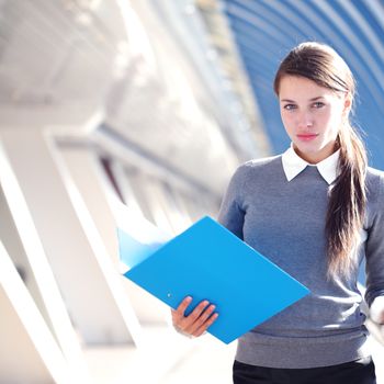 Young Businesswoman with folder standing in corridor of modern office building