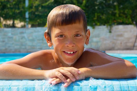 Happy sun tanned boy smiling at side of swimming pool, 8 years