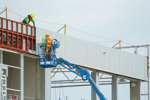 Workers in a baskets are installing sheet, building a factory.