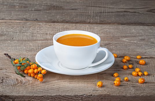 Seabuckthorn juice and berries on wooden table. Sea-buckthorn juice in a white cup on the table.