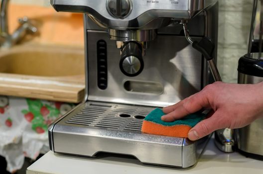 Barista cleaning coffee machine at cafe using orange sponge