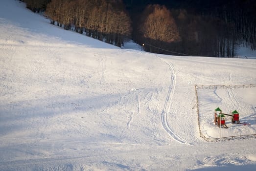 view of a snow-covered field with a fence for the children's rides with a forest in the background. Seasonal and winter concept