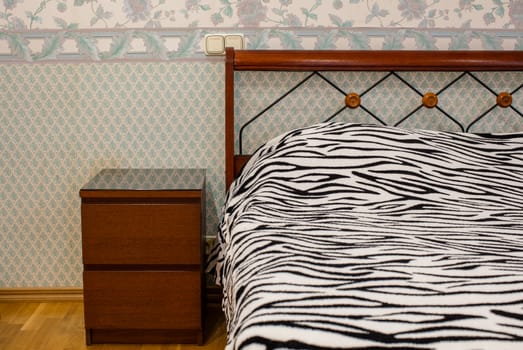 Brown wooden nightstand near double bed with zebra pattern blanket
