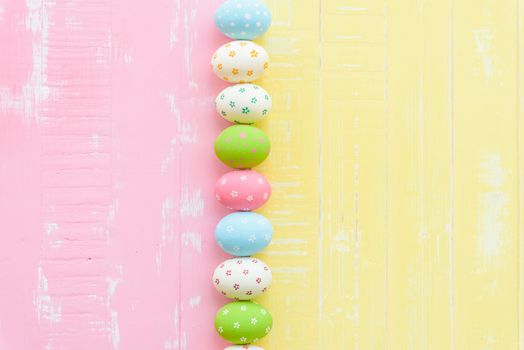 Happy easter! Row Easter eggs with colorful paper flowers on bright pink and yellow wooden background.