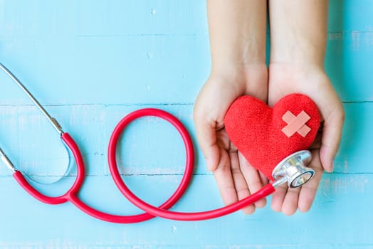 World health day, Healthcare and medical concept. Woman hand holding red heart with Stethoscope, notepad or notebook, thermometer and yellow Pill on Pastel white and blue wooden table background texture.