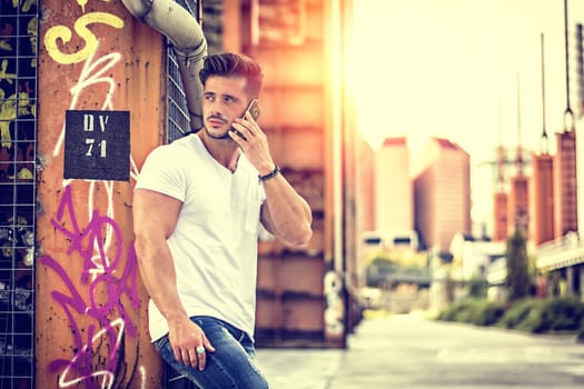 Handsome young man standing outdoors in urban environment on metal stairs, talking on cell phone