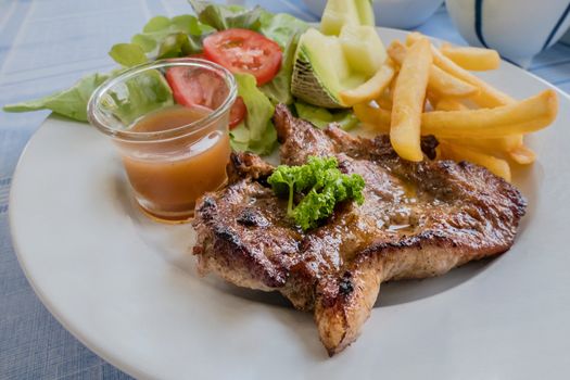 Grilled pork steak served with French fries , melon and vegetables
