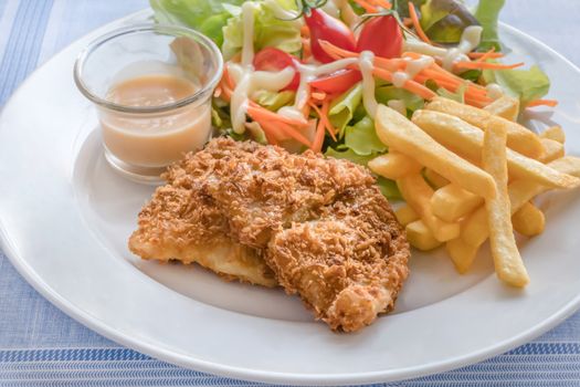 Deep fried fish steak served with french fries and fresh vegetables on white plate