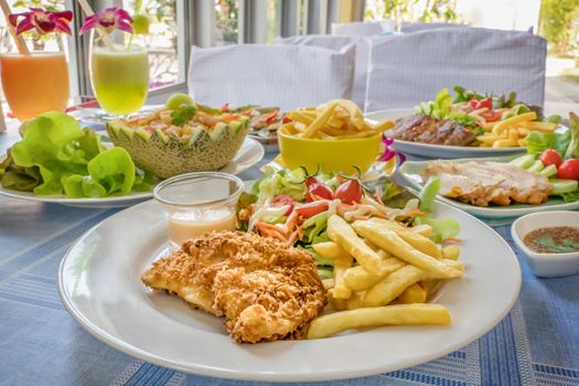 Deep fried fish steak served with french fries and fresh vegetables on plate , And  full of food on table