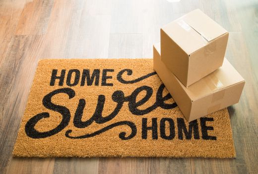 Home Sweet Home Welcome Mat On Wood Floor With Shipment of Boxes.