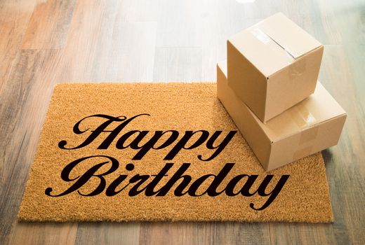 Happy Birthday Welcome Mat On Wood Floor With Shipment of Boxes.