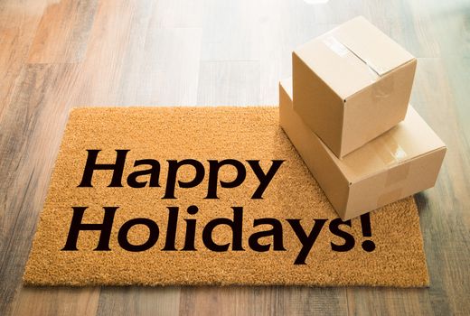 Happy Holidays Welcome Mat On Wood Floor With Shipment of Boxes.