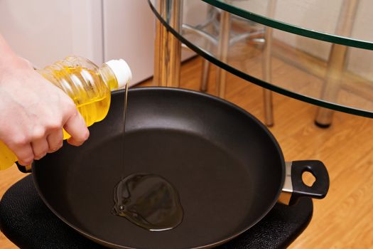 A woman pours sunflower oil from a bottle into a pan for making pies.