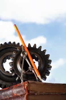 Divider near gears on stack of old books against blue sky background