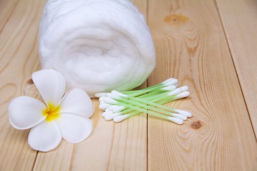 White cotton bud with cotton roll and white flower over wooden table background