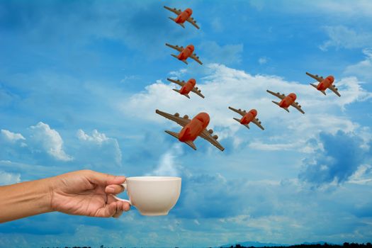Hand holding coffee cup with airplane models on sky background, Travel planning concept.