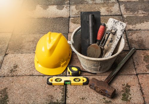 Construction tools or safety equipment with yellow helmet on brick ground