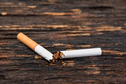Cigarette divided into two parts on wooden background