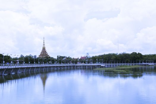 The temple reflected on the water under the blue sky with white cloudy in Thailand.