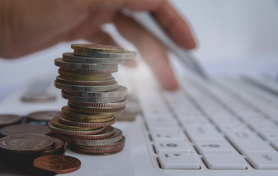 stack coins on white laptop and finger press button on keyboard. Financial and saving concept.