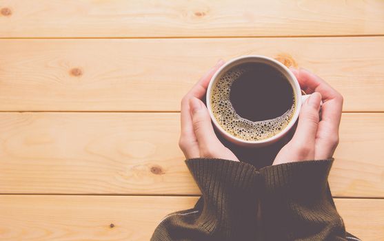 Female hands holding a cup of coffee over wooden table. Top view.