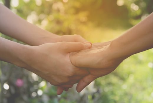 Hand of lady and younger lady holding together on nature background