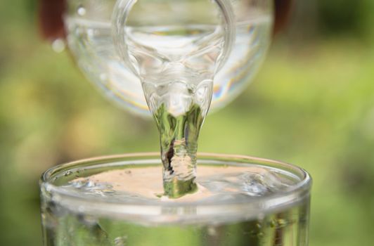 Person pouring water from bottle to glass on nature background