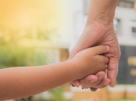 Close up of mother and a child hands at the sunset. Mother holding a hand of son in summer day outdoors.