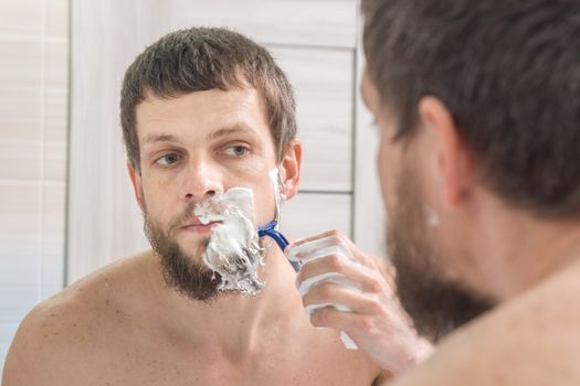 A man shaves his beard very strong