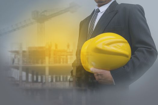 Businessman or safety officer holding yellow helmet with the building is background in construction site.