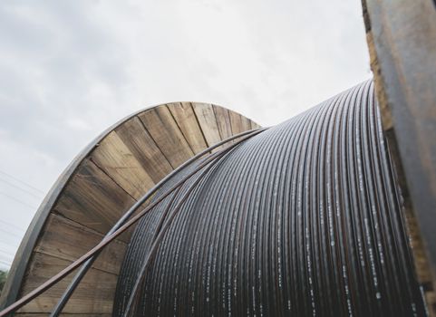 black wire  electric cable with wooden coil of electric cable under the sky.