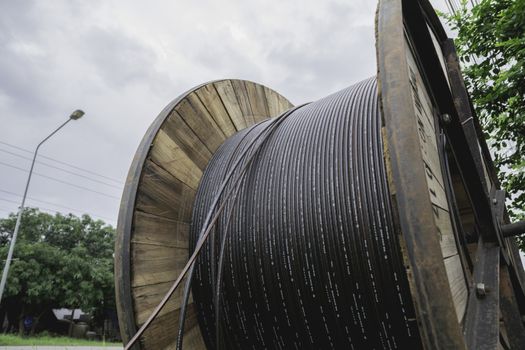 black wire  electric cable with wooden coil of electric cable under the sky.