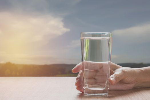 hand holding a glass of pure water. Hand holding a glass of water on table with blue sky background.