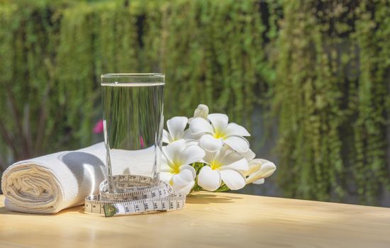 glass of water on a wooden table with white flower and handkerchief on nature background.