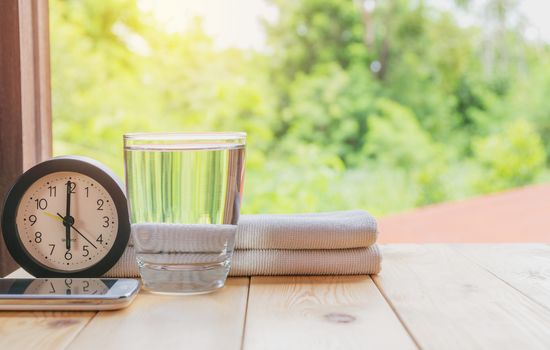 glass of water on a wooden table with clock and handkerchief on nature background.