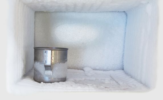 Stainless steel drinking water glass in freezer of a refrigerator. Ice buildup inside of a freezer walls.