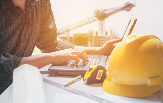 Architect engineer using laptop for working with yellow helmet, laptop and coffee cup on table.