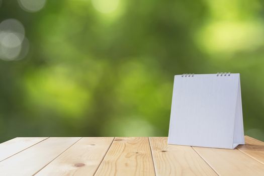 White calendar on wood table on nature background and copy space mock up.