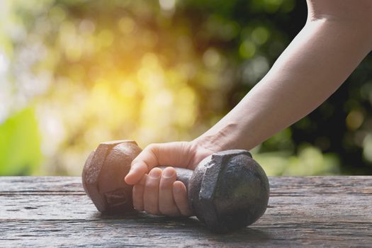 Hand of person holding dumbbell for exercise and healthy under the sunlight.